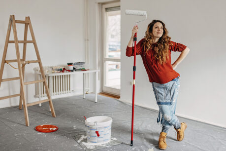 Woman holding paint roller looking proud of freshly painted room