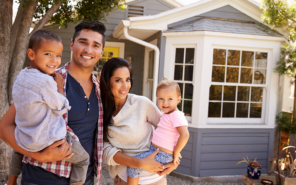 Man and woman couple standing outside their home holding their two children