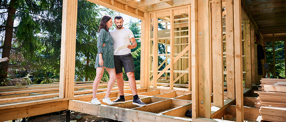 Man and woman couple walking through home construction and discussing building plans