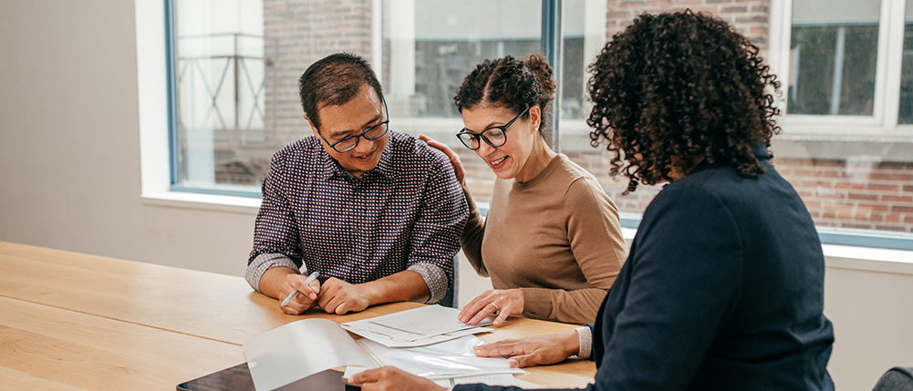 Couple smiling while discussing and reviewing documents with advisor