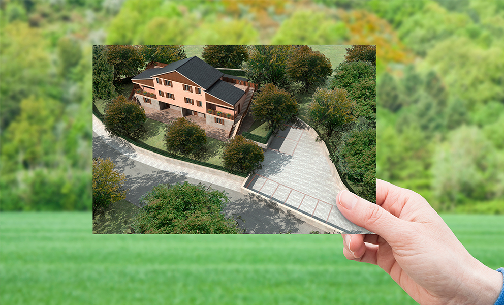 Hand holding up image of new home in front of an open area of land