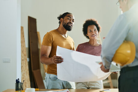 Man and woman copule smiling while reviewing blueprints with builder