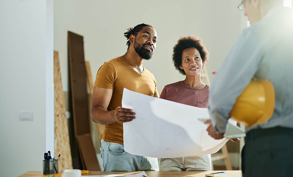 Man and woman copule smiling while reviewing blueprints with builder