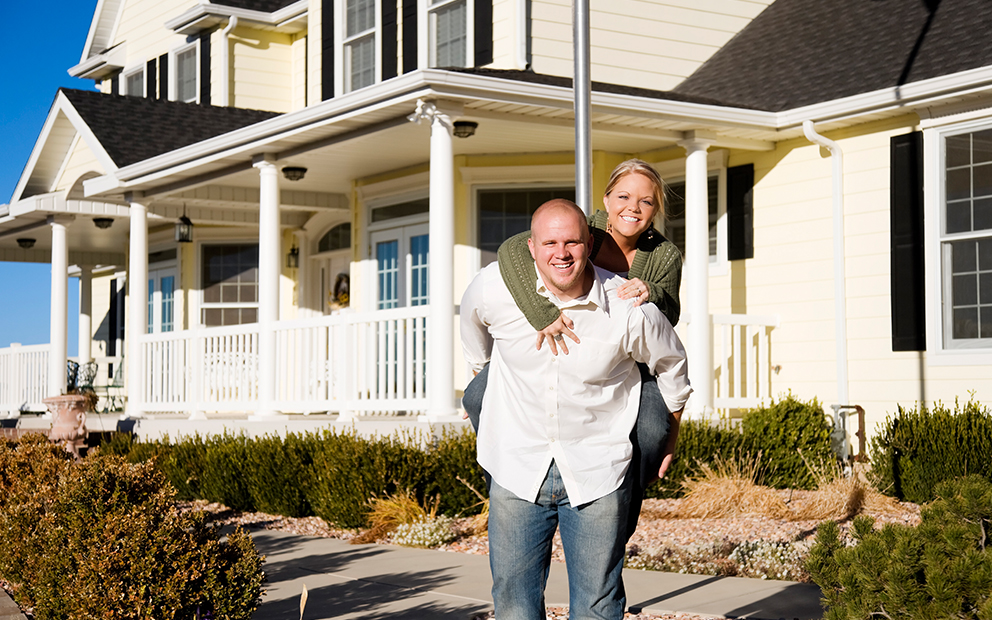 Man holding woman partner on his bag while standing in front of home