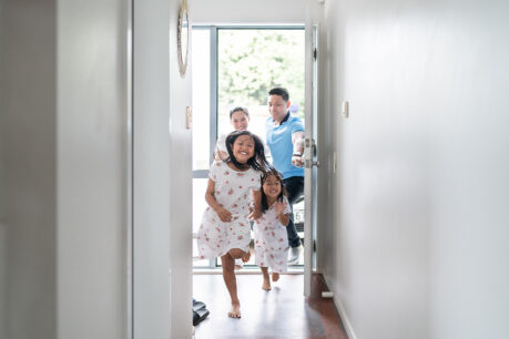 Two sisters running through the doorway of their new home with their mom and dad