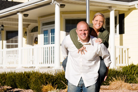 Man holding woman partner on his bag while standing in front of home