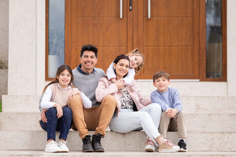 Family sitting and smiling on steps leading up to their new home