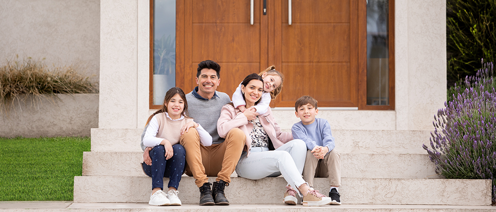 Family sitting and smiling on steps leading up to their new home