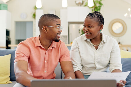 Man and woman coupling sitting on couch while smiling and discussing over laptop