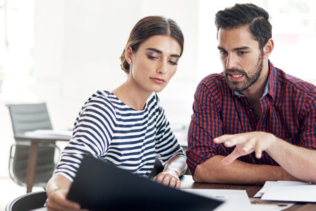 Man and woman sitting together at table while reviewing and discussing documents