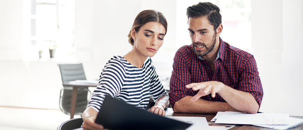 Man and woman sitting together at table while reviewing and discussing documents