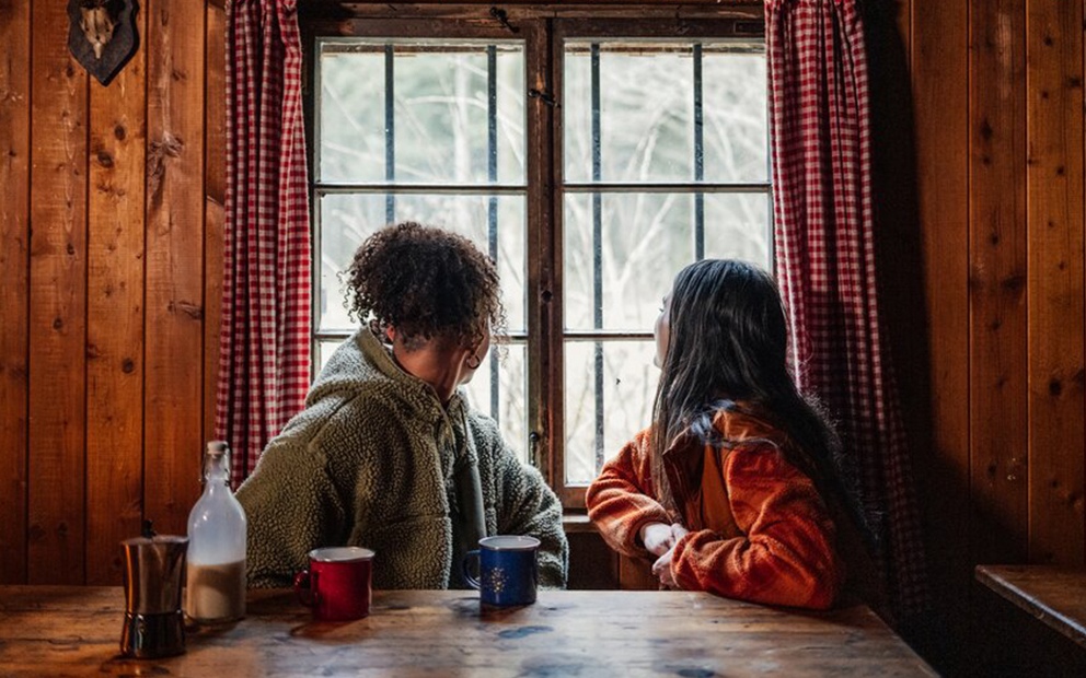 Couple sitting at table inside log cabin as they look out the window