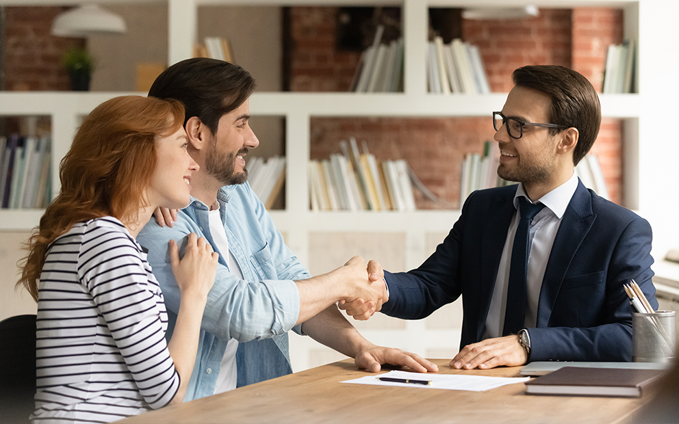 Couple discussing with advisor while smiling and shaking hands