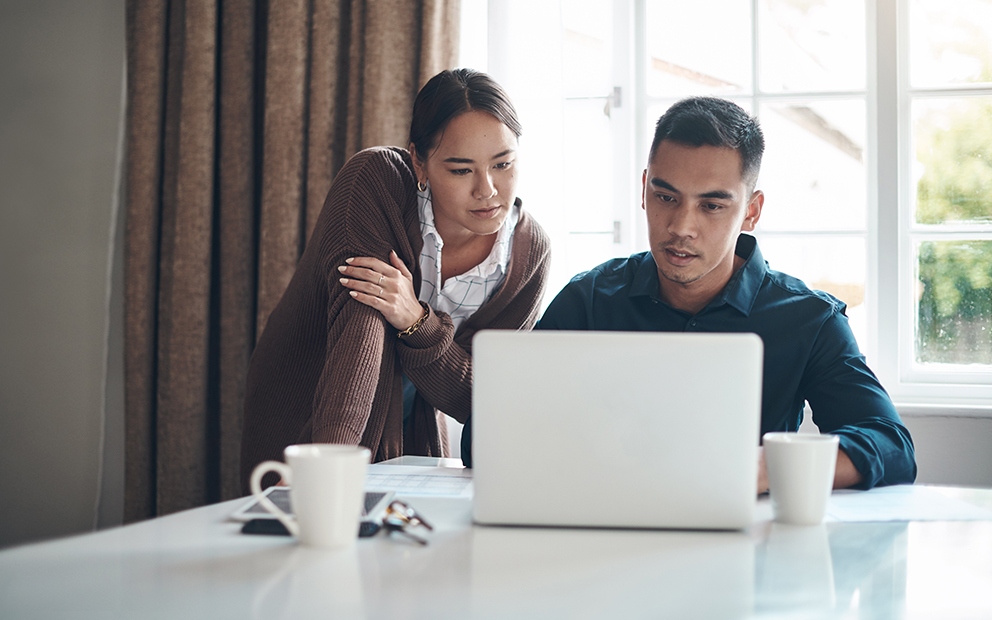 Couple reviewing documents on laptop while sitting at table