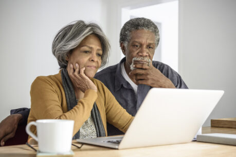 Couple sitting together at kitchen table while looking at their laptop