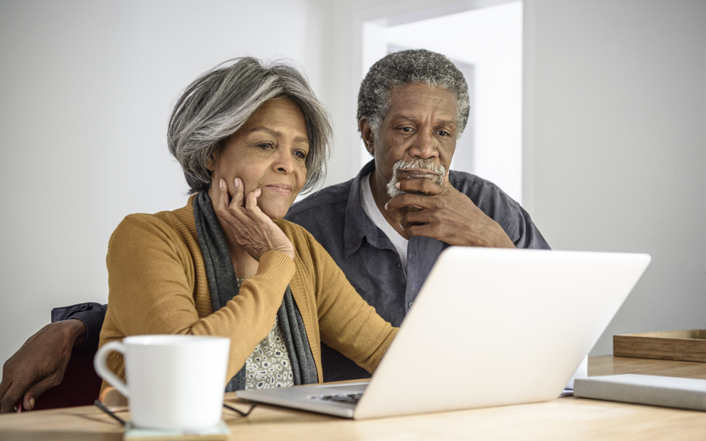 Couple sitting together at kitchen table while looking at their laptop