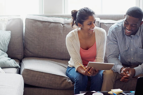 Couple sitting on couch and smiling while discussing over laptop