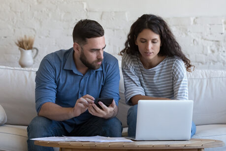 Couple sitting on couch together while looking at laptop