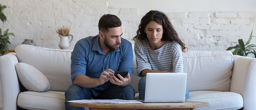 Couple sitting on couch together while looking at laptop