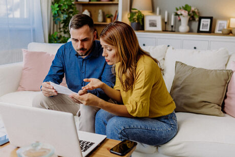 Couple sitting on couch together while look over documents with confusion and concern