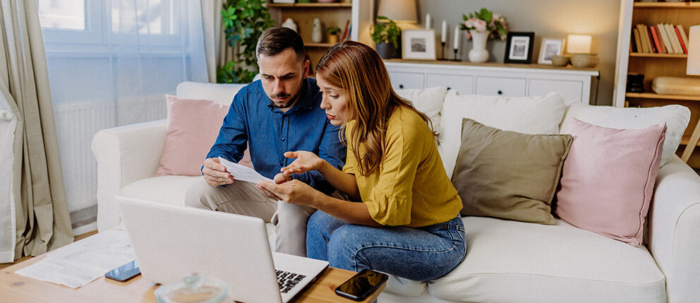 Couple sitting on couch together while look over documents with confusion and concern