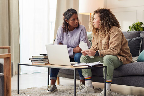 Couple sitting on couch together while looking concerned about documents in front of them