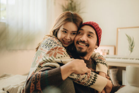 Man and woman couple sitting on floor in living room together while hugging and smiling