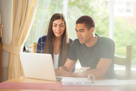 Couple sitting at table together while they review documents on laptop