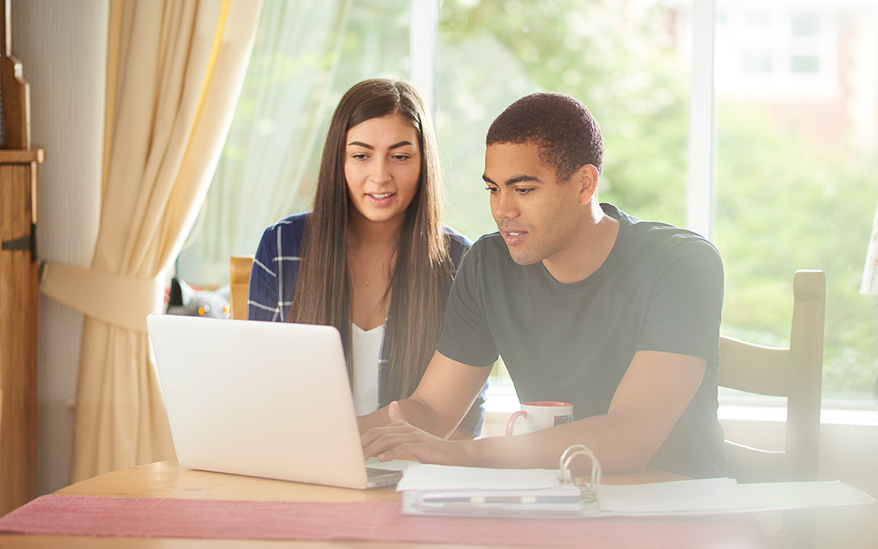 Couple sitting at table together while they review documents on laptop