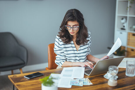 Woman sitting at home desk looking over laptop and documents