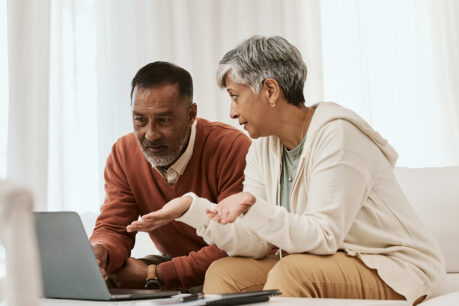 Couple sitting together on couch while they look over and discuss over laptop