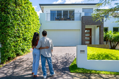 Couple holding each other while they stand at the end of a driveway and look at a house