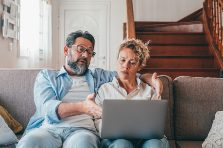 Couple sitting together on couch while looking at and discussing over laptop