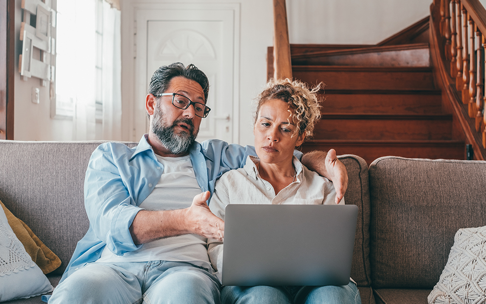 Couple sitting together on couch while looking at and discussing over laptop